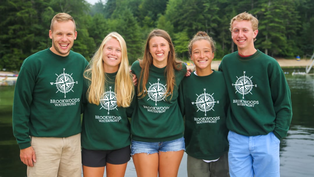 Five camp staff wearing Brookwoods sweatshirts by the lake