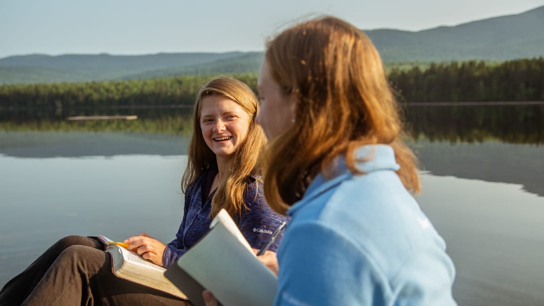 two girls reading bibles by the lake