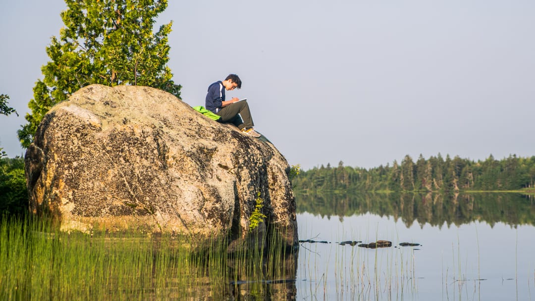 Camper reading a book on a rock for bible study