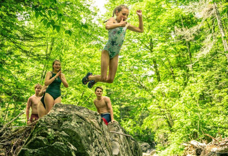 Girl jumping off rock into a river at Moose River Outpost