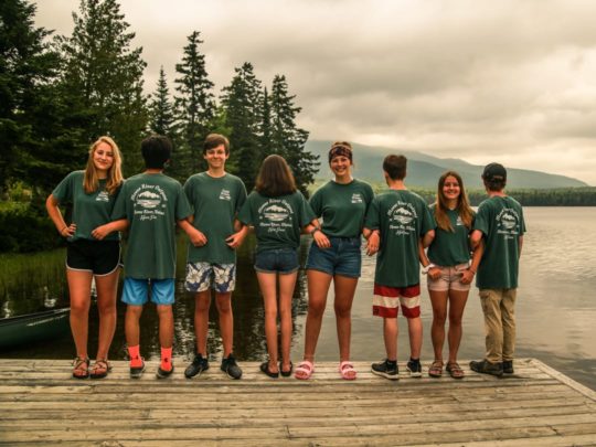 Campers wearing matching shirts and linking arms by the lake