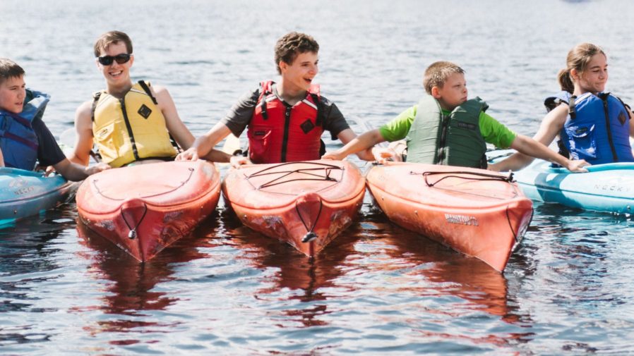 Five campers in kayaks holding onto each other and smiling