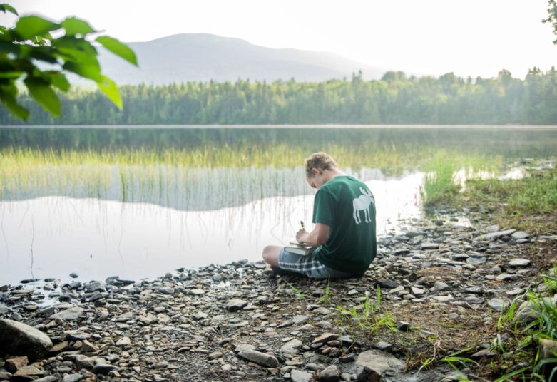 Male camper writing by lake at MRO