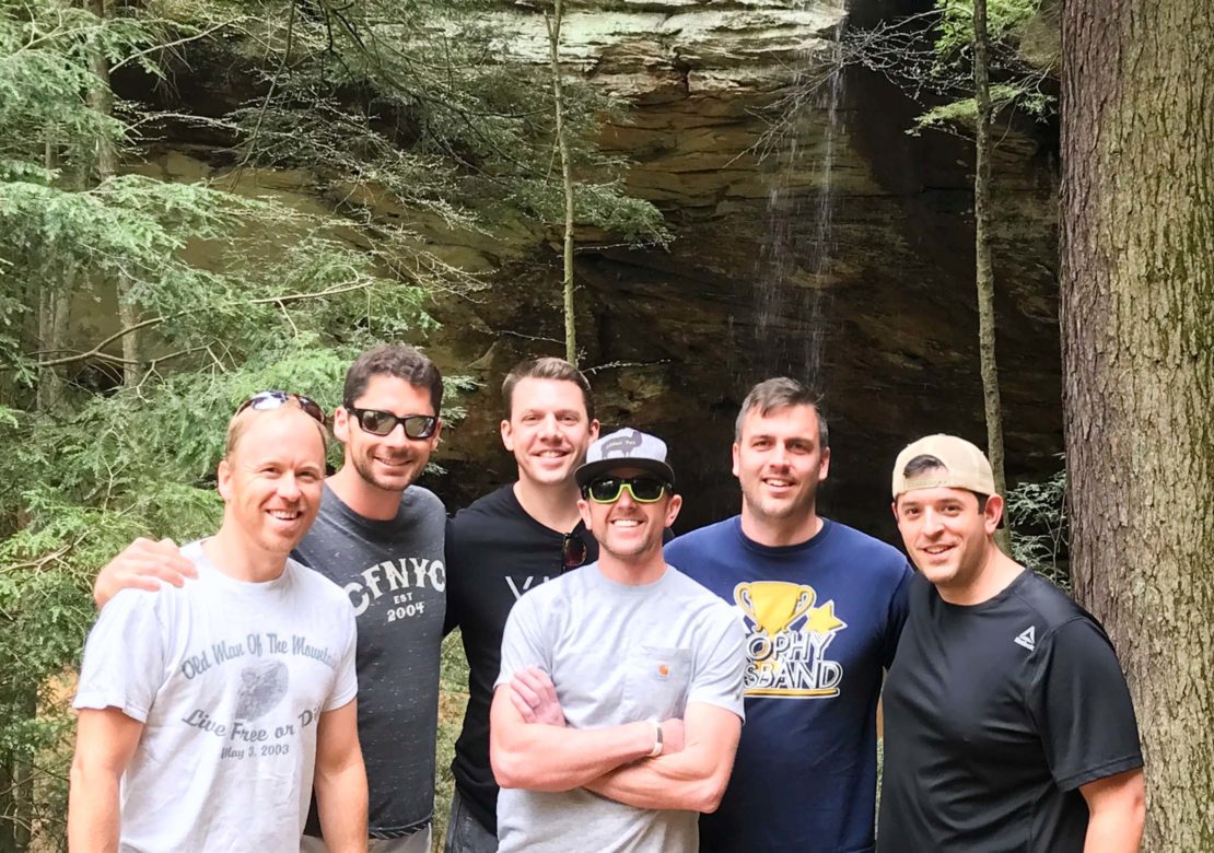 Group of male almuni standing by waterfall