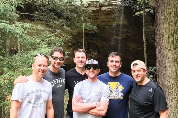 Group of male almuni standing by waterfall