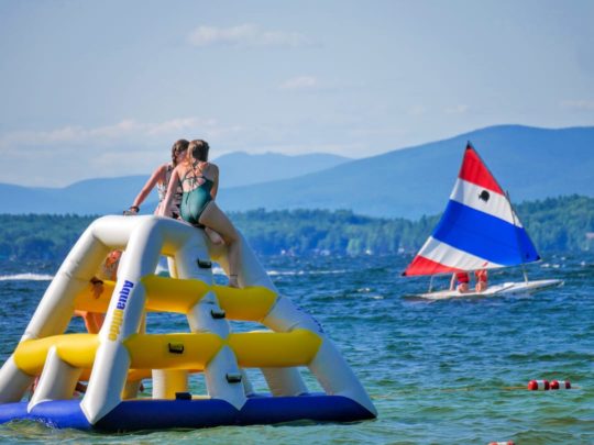 girls sitting on inflatable jungle gym looking at a sailboat